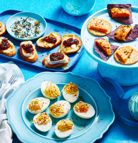 Holiday snacks of devilled eggs, cheese ball slices on chips, and brie with cranberries on decorative blue serving platters