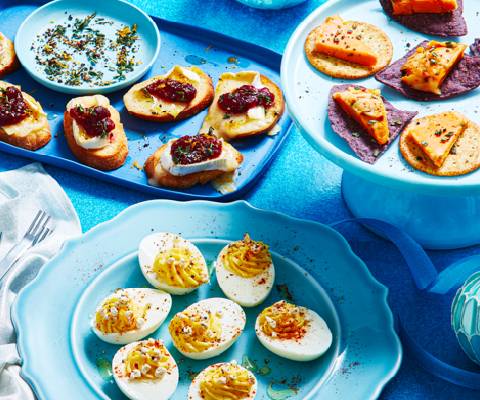Holiday snacks of devilled eggs, cheese ball slices on chips, and brie with cranberries on decorative blue serving platters