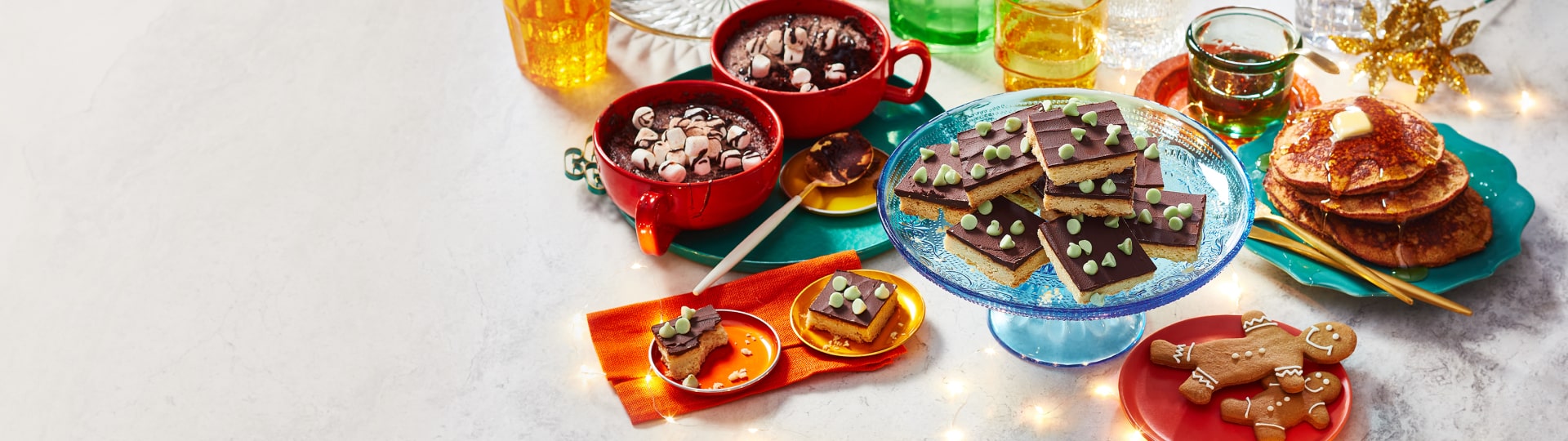 Marble surface with twinkle lights and holiday décor, plus three easy baking mix desserts: gingerbread banana bread pancakes, hot chocolate mug cakes and mint chocolate shortbread cookie slices