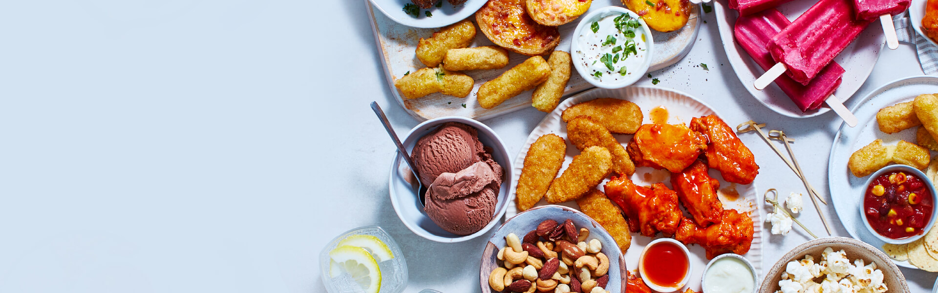 Game-day table set up with pretzels, chips, ice cream, potato skins, meatballs, mozzarella sticks, and ice cream pops.