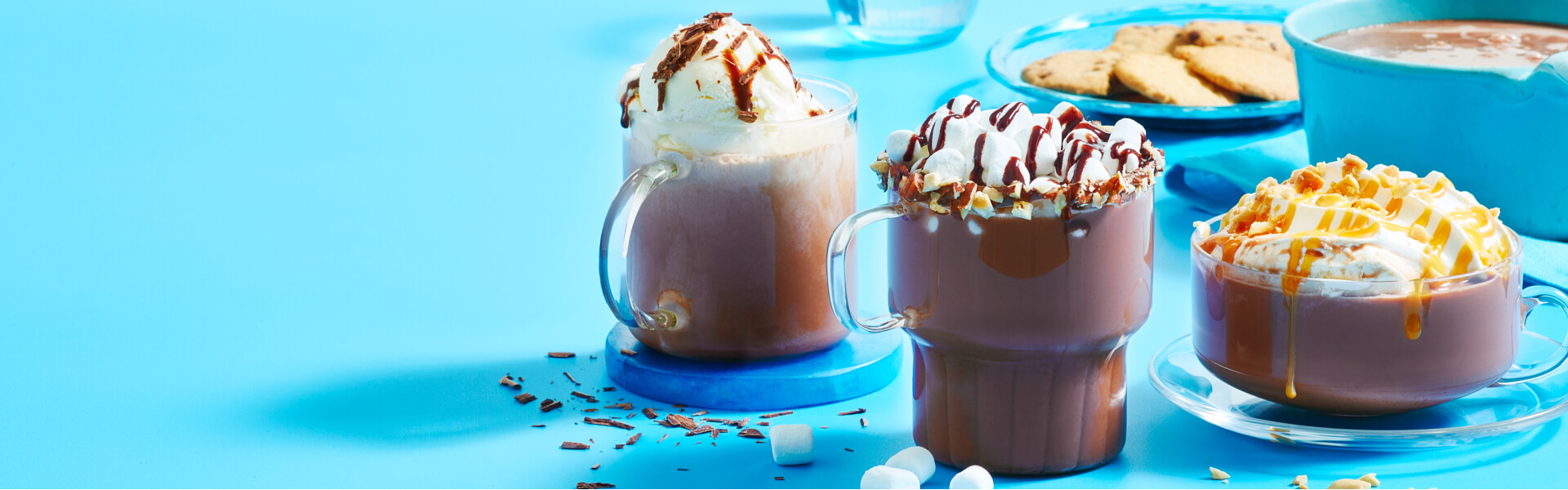 3 clear heat-proof mugs filled with different flavours of hot chocolate and toppings