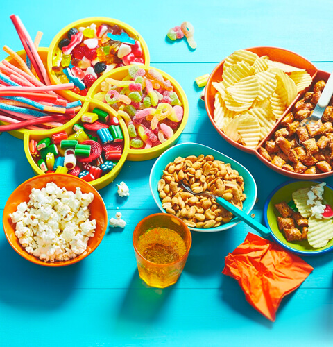 Aqua table surface with variety of movie snacks: popcorn, sweet and sour candy, chips, pretzel bites and flavoured sparkling water