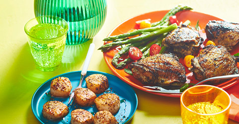 yellow background with two dinner plates, one with tea-seared scallops and one with tea-rubbed chicken thighs