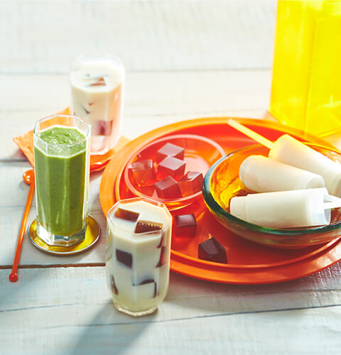 reinvent_tea white-washed wooden table with orange tray with chai ice pops, jelly tea cubes and two tea-flavoured cold drinks to the side