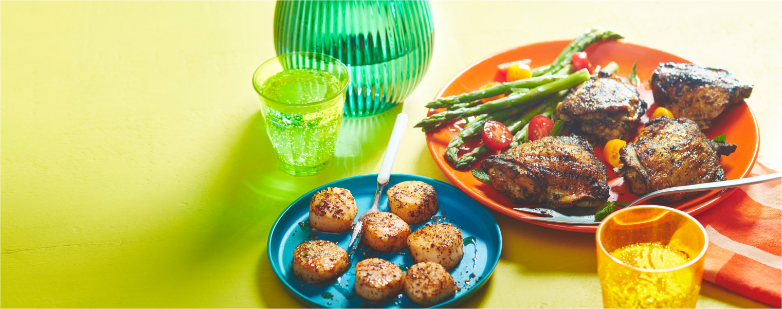 yellow background with two dinner plates, one with tea-seared scallops and one with tea-rubbed chicken thighs