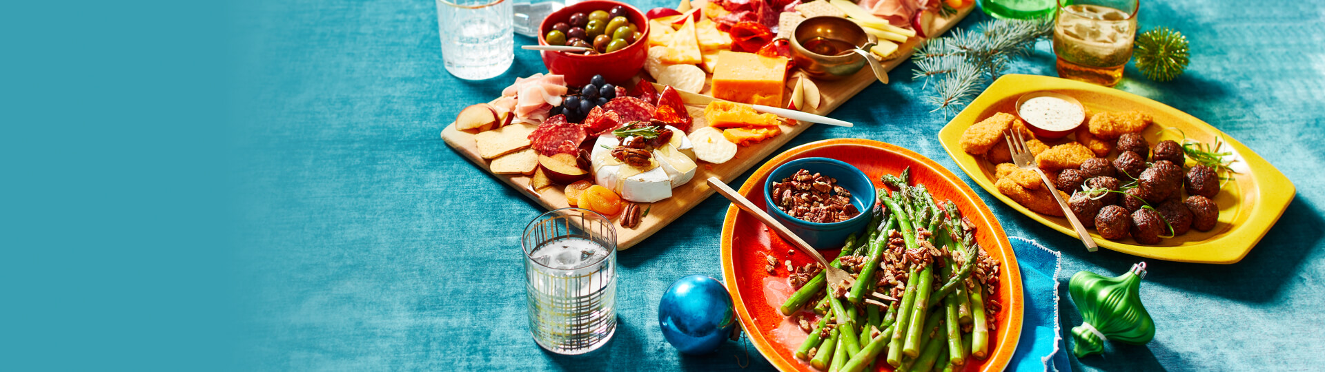 Dark aqua tablecoth with platters of food - a charcuterie board, a mixed appetizer plate, nut-topped green beans, and a plate with plant-based meatballs and chickenless chicken strips.