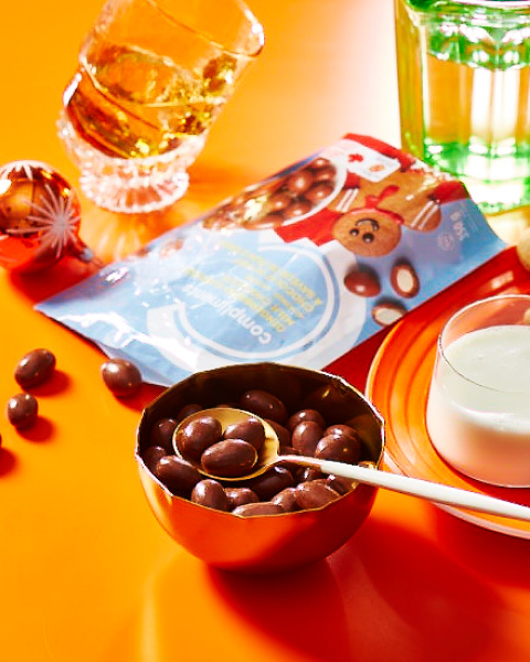 Orange surface with a package and bowl of gingerbread flavour milk chocolate coated almonds