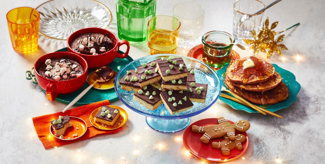 Marble surface with twinkle lights and holiday décor, plus three easy baking mix desserts: gingerbread banana bread pancakes, hot chocolate mug cakes and mint chocolate shortbread cookie slices