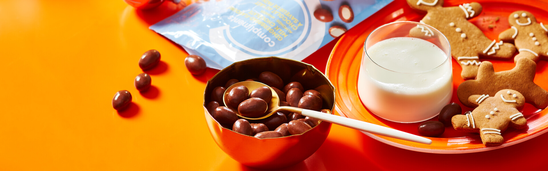 Orange surface with a package and bowl of gingerbread flavour milk chocolate coated almonds