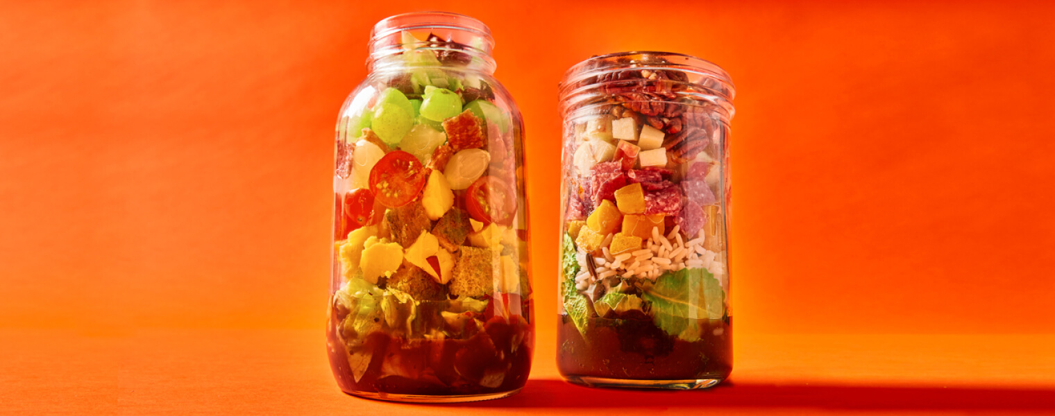 two large jars of layered salad on an orange background