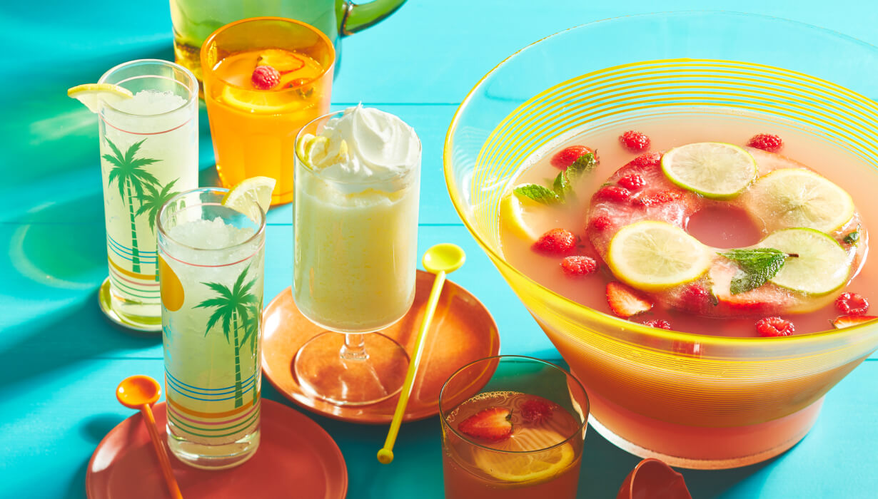 aqua blue picnic table surface with a tray of lemonade drinks next to a bowl of punch with a frozen lemonade ring chilling it