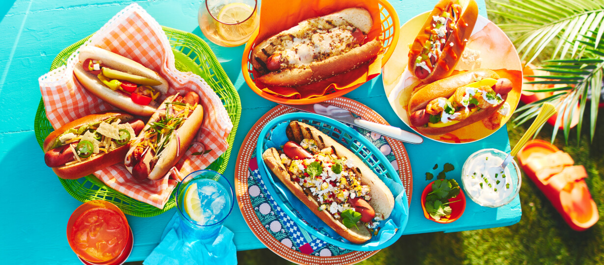 Blue tabletop with 4 plates of the 7 hot dogs.