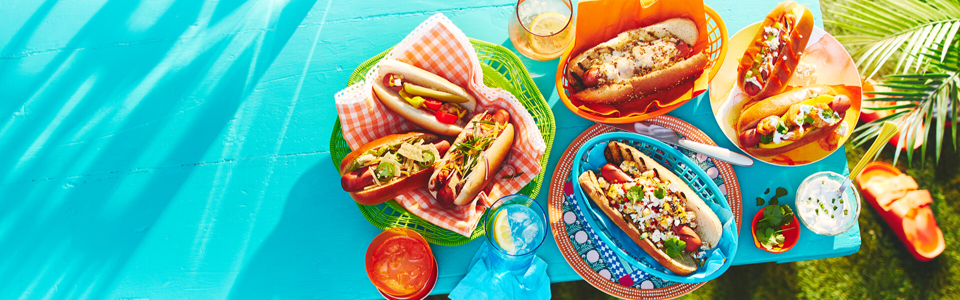 Blue tabletop with 4 plates of the 7 hot dogs.