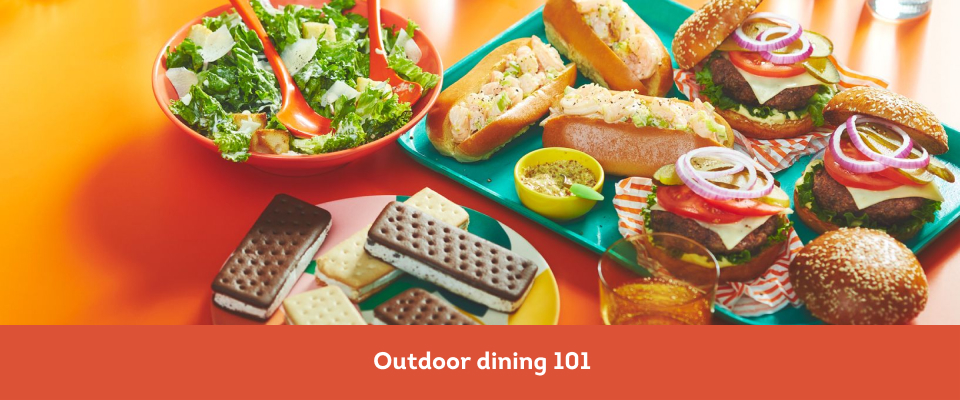 orange surface with bowl of caesar salad, shrimp rolls, and ice cream bars for an outdoor dinner