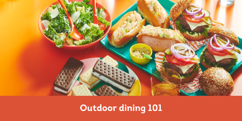 orange surface with bowl of caesar salad, shrimp rolls, and ice cream bars for an outdoor dinner