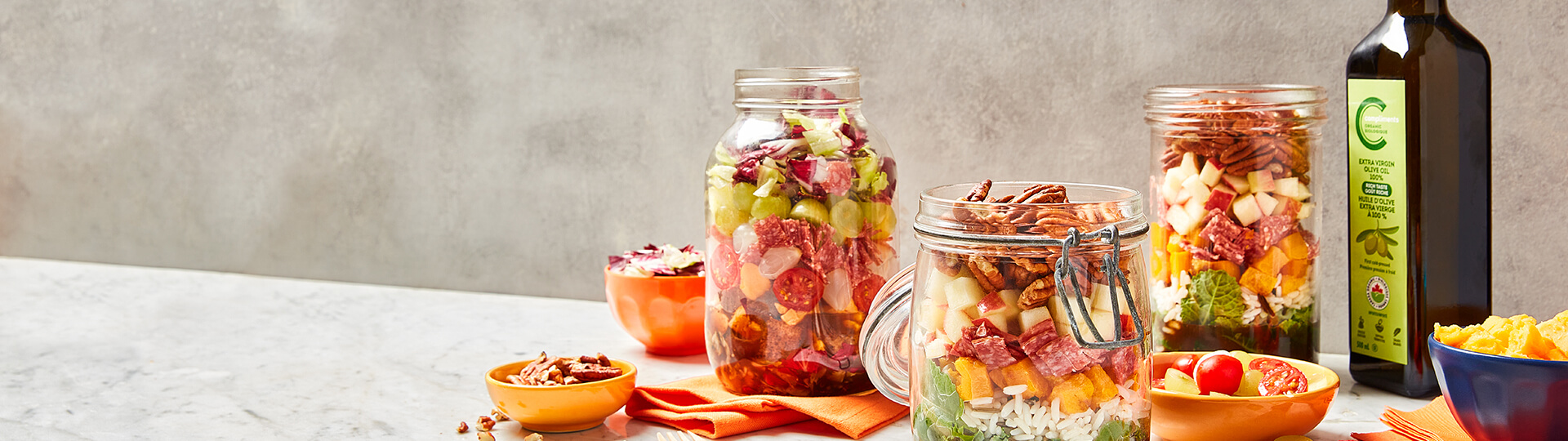 marbled background and surface with jars of salad to go, olive oil, tomatoes, cheese and nuts.