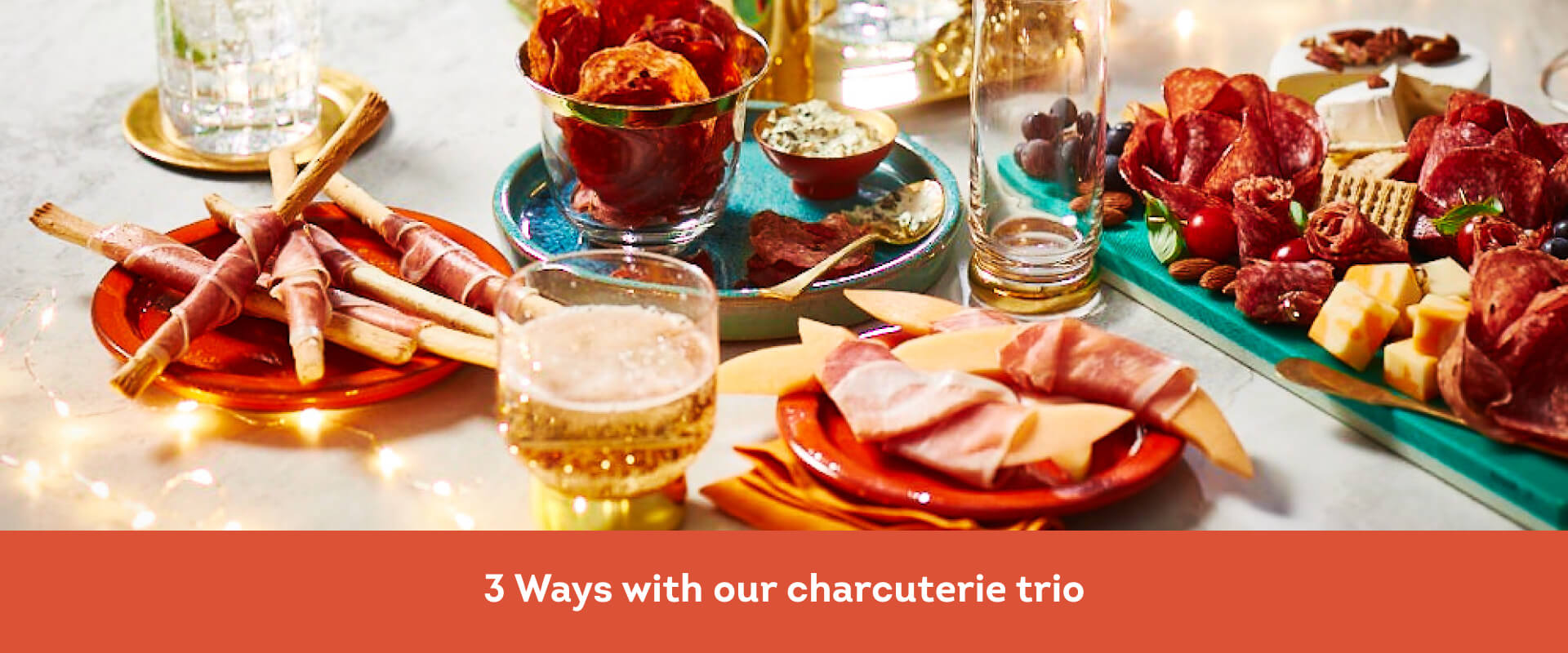 Marble table with twinkle lights, a charcuterie board, plate of salami chips, and prosciutto-wrapped melon and breadsticks.