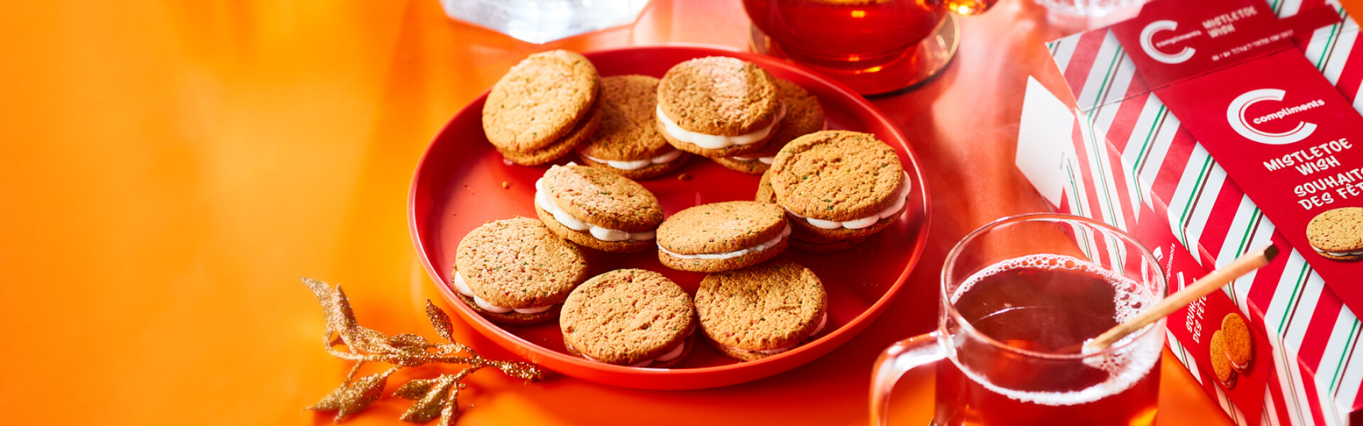 Plate of Compliments Mistletoe wish cookies beside a cup of cider and a box of the cookies