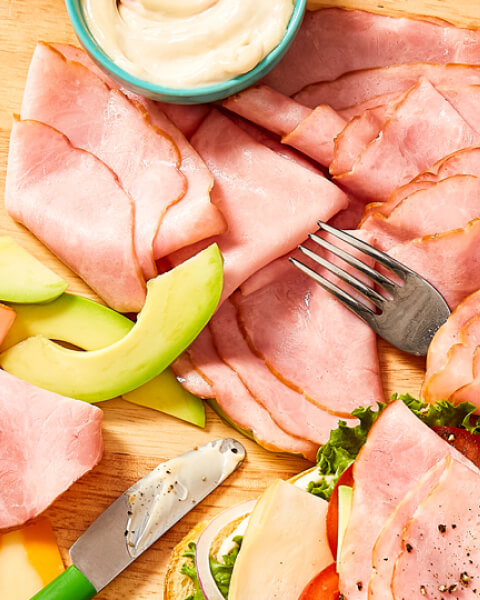 Overhead shot of all natural deli-meats on cutting board with sliced avocados