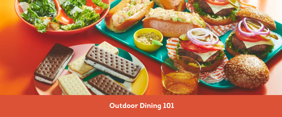 Orange surface with platters of food: shrimp rolls, burgers, caesar salad and ice cream bars