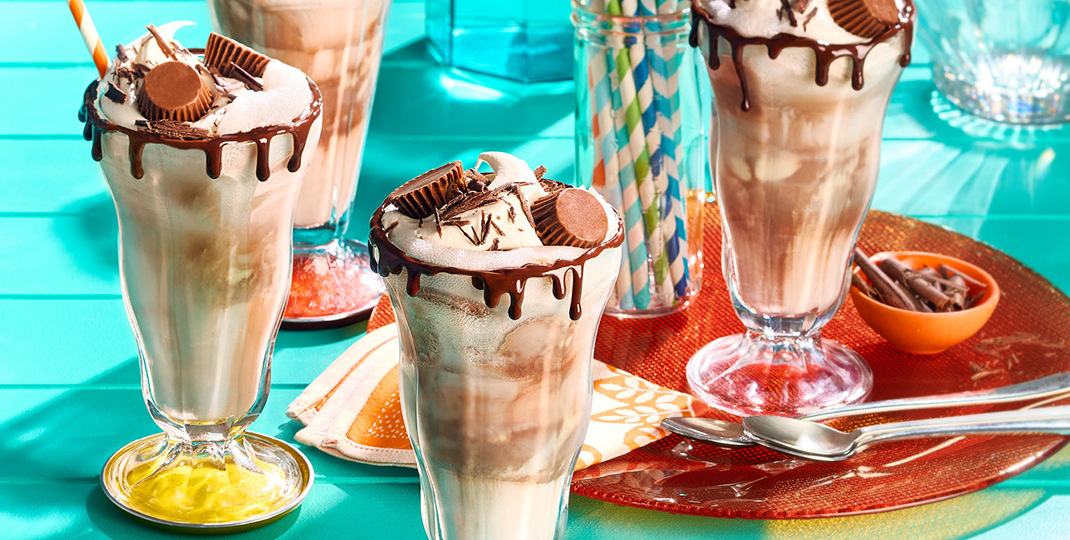 Four chocolate and peanut butter floats in tall glasses with straws and spoons.